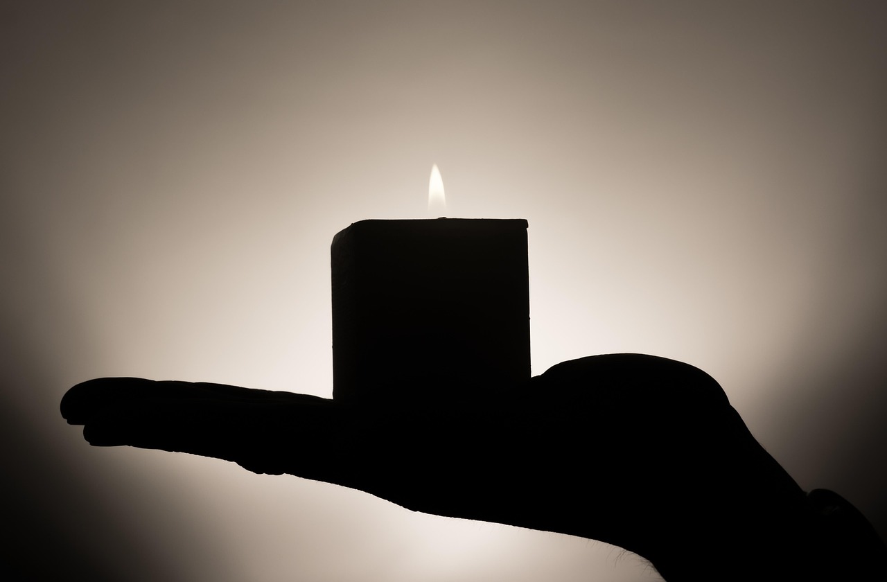 A lit candle held on an open palm against a soft backlight